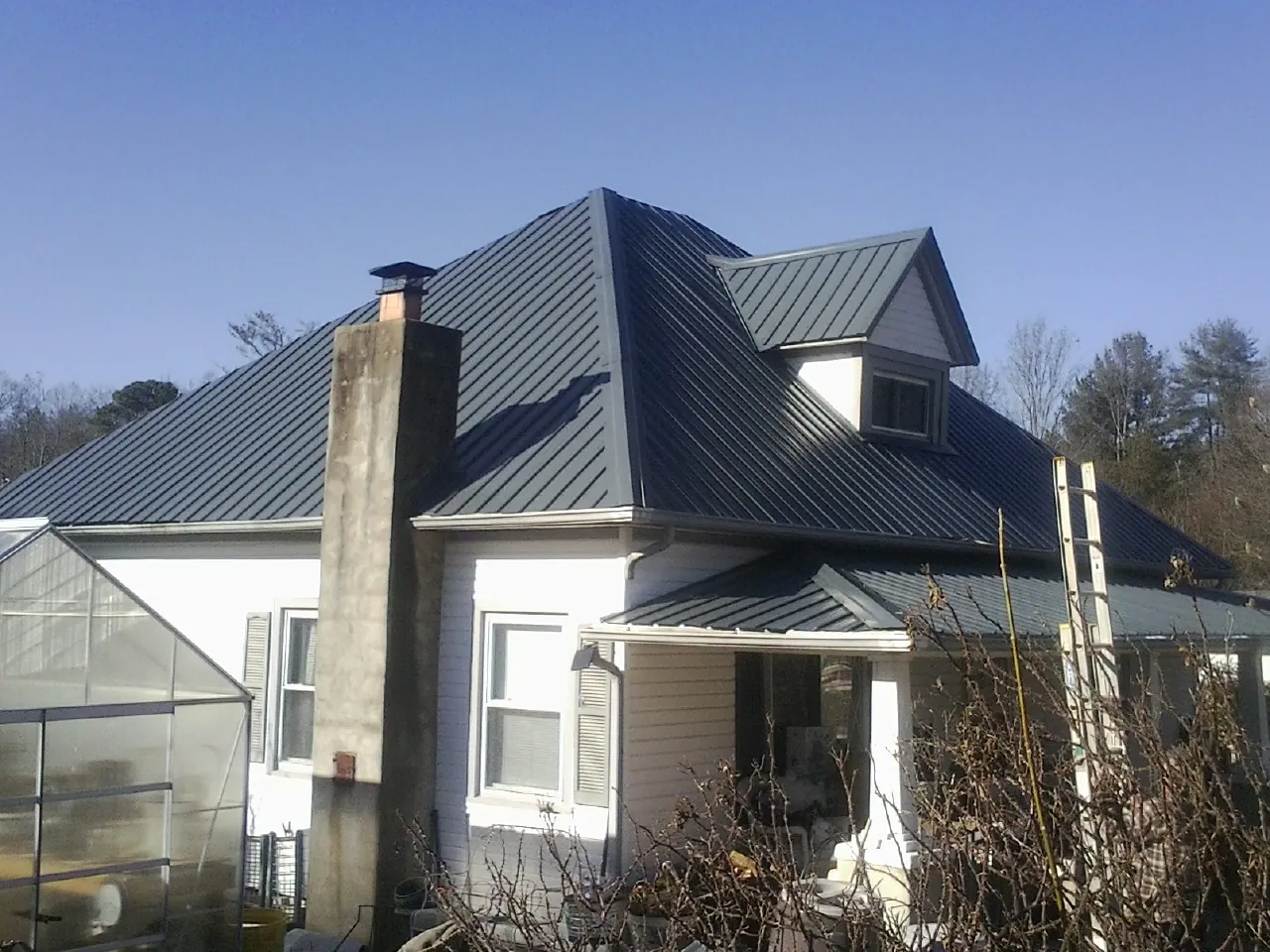 Dark blue standing seam metal roof on a white farmhouse with dormer — Slate & Tile Roof Repair by Roofing Brothers in Earlysville