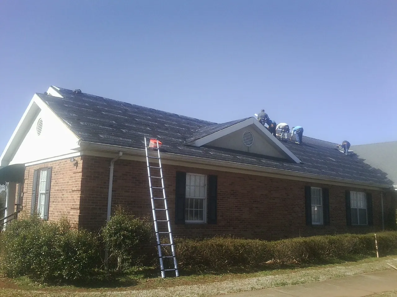 Crew tearing shingles off a brick ranch roof with a ladder set — Emergency Roof Repair work by our crew in Earlysville