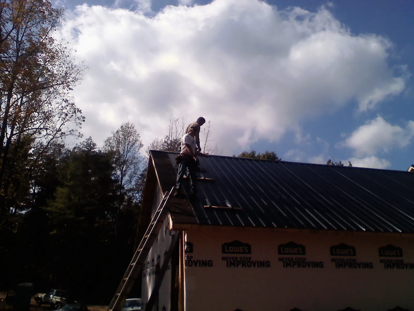 Roofer fastening dark metal panels high against a cloudy sky, from a Roof Inspection job in Earlysville