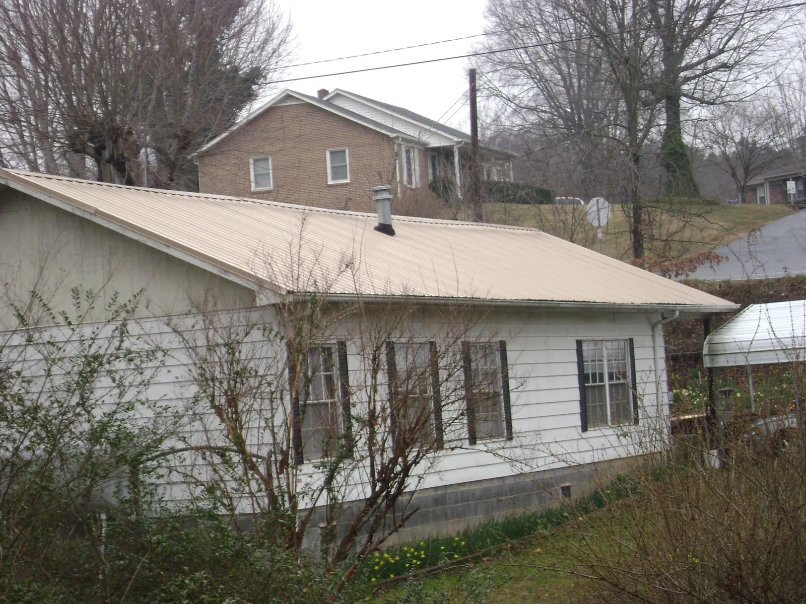 Tan metal roof on a white sided house set into a hillside — Commercial Roofing by Roofing Brothers in Earlysville